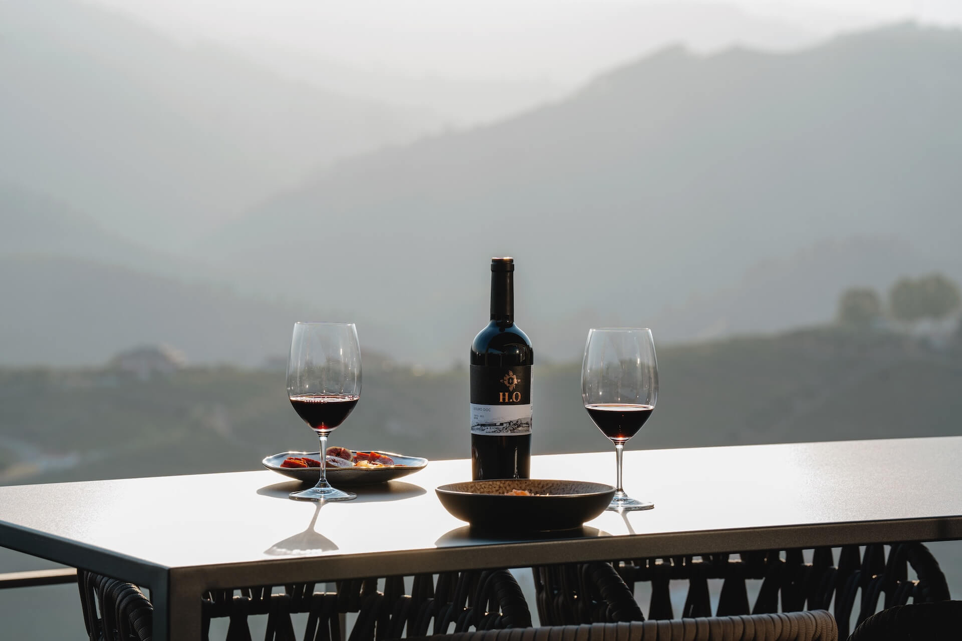 Vista da Adega da Horta Osório, com uma garrafa de vinho H.O Tinto e dois copos numa mesa